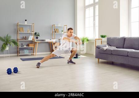 Fit young man doing side lunge stretching exercises during sports workout at home Stock Photo