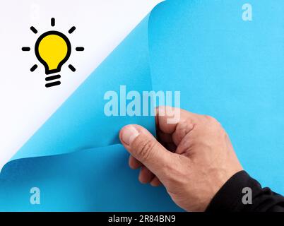 To find a creative idea or a new invention concept. Male hand opens the blue paper and reveals the idea light bulb symbol. Stock Photo