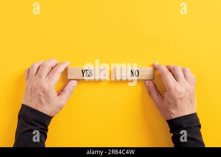 Making the right decision. Rejecting or accepting. Political choice. Hands holding wooden blocks with the words yes and no. Stock Photo
