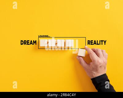 Transition of dreams into reality. Realizing the dreams. Hand places a wooden cube to the loading bar with the words dream and reality. Stock Photo
