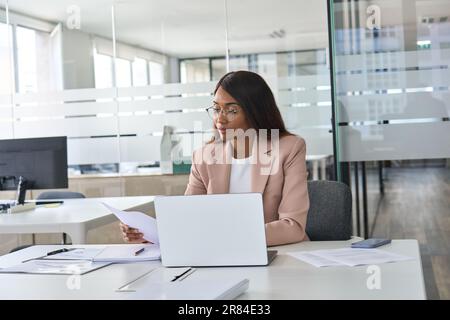 Busy young business woman executive reading papers working on laptop in office. Stock Photo