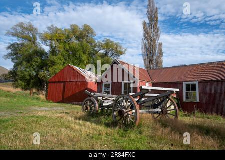 Derelict wooden wagon in front of red barn, St James Station near Hanmer Springs, Canterbury, South Island, New Zealand Stock Photo