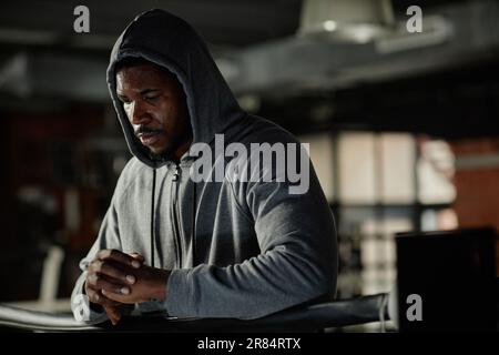 Young African American sportsman in grey hoodie standing in front of camera in boxing club and thinking of forthcoming training Stock Photo