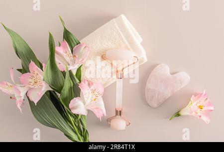 A beautiful composition of a set of skin care products for the face and decalte area. Rose quartz roller on terry towel, gouache. Top view Stock Photo