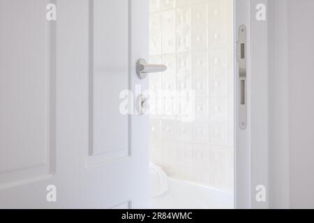 White bathroom door left ajar, slightly open doorway with modern handle, selective focus Stock Photo