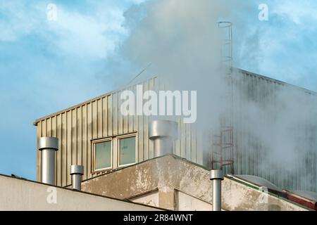 Industrial chimney fume and steam exhaustion on old factory building, selective focus Stock Photo