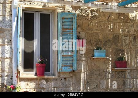 A stonewall and window with blue wooden shutters decorated with flower pots. Stock Photo