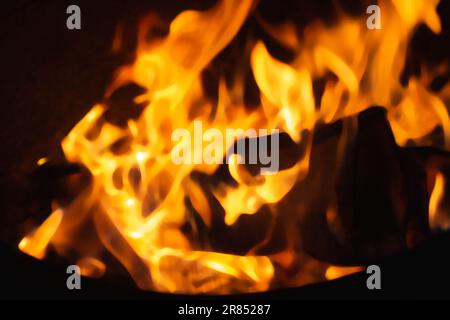 Blurred background with Burning firewood in the fireplace close up.Defocused or blurred image. Fire burns in the fireplace. Black logs burned down. He Stock Photo