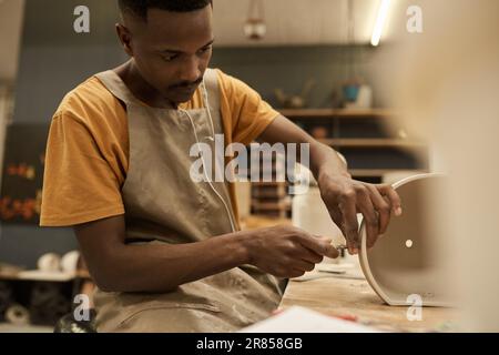 Young African ceramist making holes in a pot at a bench in a workshop Stock Photo