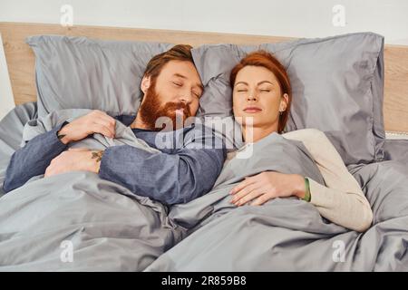 parents alone at home, quiet house, redhead husband and wife sleeping in cozy bedroom, bearded man and carefree woman relaxing on weekends, day off, t Stock Photo
