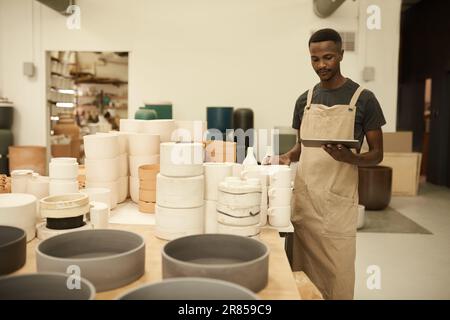 African potter doing inventory using a tablet in a ceramics workshop Stock Photo