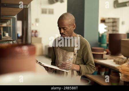 African potter taking inventory of pots on shelves in a ceramics workshop Stock Photo