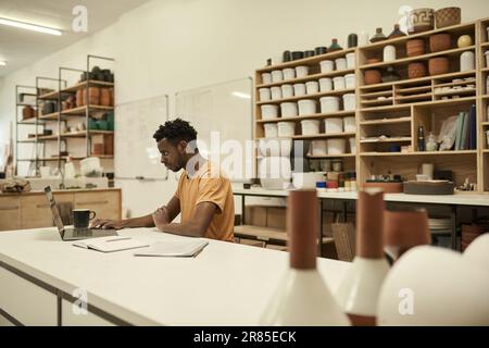 African ceramics workshop manager using on a laptop at a table Stock Photo