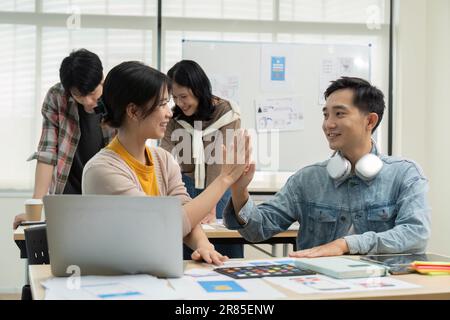 Group of Asia young creative people celebrating giving five after working for UX UI design completed feeling happy. Coworker teamwork concept Stock Photo