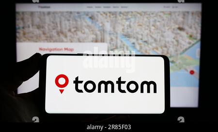 Person holding smartphone with logo of Dutch location technology company TomTom N.V. on screen in front of website. Focus on phone display. Stock Photo