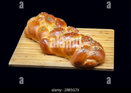 A white challah loaf on a wooden board with linseeds, sunflower seeds and pumpkin seeds. Golden freshly baked crust with highlights. Stock Photo