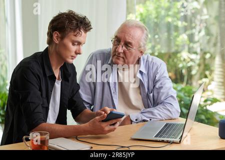 Senior man listening to grandson explaining how to use application on smartphone Stock Photo