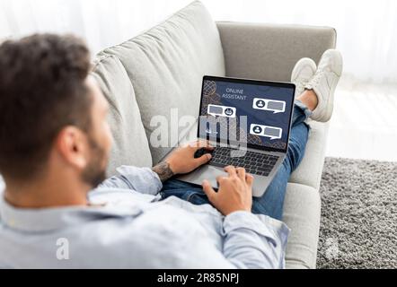 Unrecognizable man sitting on couch, using laptop with Online Assistant Stock Photo