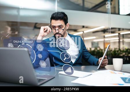 Middle eastern businessman wearing eyeglasses working on laptop, using chatbot Stock Photo