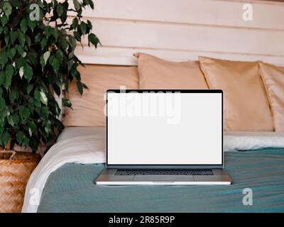 Laptop blank screen on bed in country house bedroom interior background, mockup, template. Clipping path device screen. Silver aluminium laptop at bed near green waringin tree in scandinavian country house Stock Photo