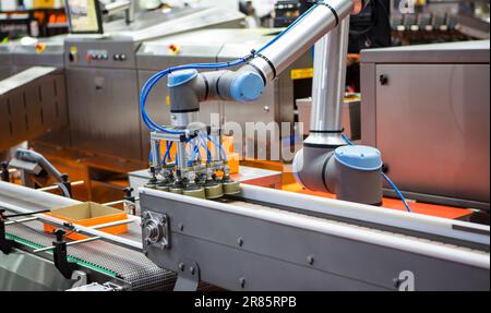 Automated robot arm lifting food can to conveyor belt in food industry. Stock Photo