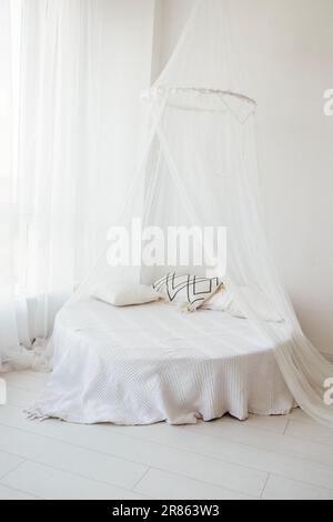 Bright stylish interior of the bedroom with a round bed and pillows. There is a canopy of light translucent fabric over the sofa. Panoramic window at Stock Photo