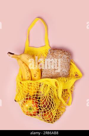 Yellow mesh string bag full of products on pink. International plastic free day background, shopping concept. 3rd of July. Copy space Stock Photo