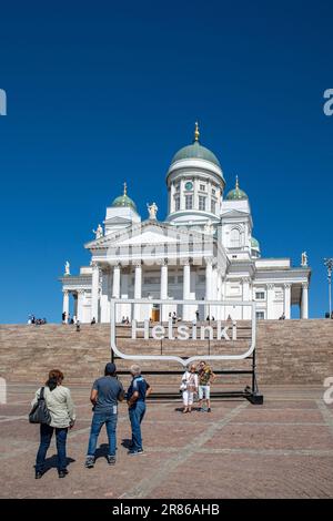 Tourists posing in front of Helsinki logo sign and Helsinki Cathedral at Senate Square in Helsinki, Finland Stock Photo