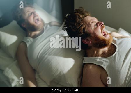 Double exposure of young mad man in vest screaming loudly in horror or during agony while lying on bed in ward of mental hospital Stock Photo