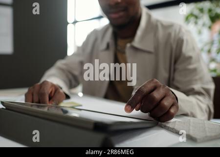 Focus on hand of young African American employee pointing at tablet screen while making presentation of scrolling through online data Stock Photo