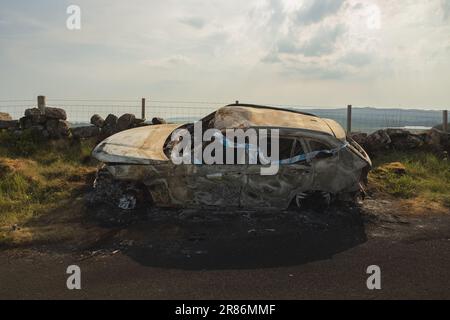 Scene of an auto accident with police tape on a burnt car wreck on a country road in the Lomond Hills Regional Park, Fife, Scotland, UK. Stock Photo