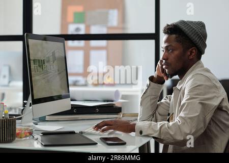 Young serious male architect or designer looking at graphic sketches on computer screen while working over new architectural project Stock Photo