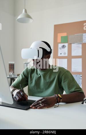 Young black man in green t-shirt creating new computer games or website while sitting in front of computer and using touchpad and stylus Stock Photo