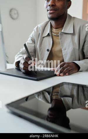 Close-up of young black man sitting by workplace in front of computer screen in office and drawing graphic sketches or retouching images Stock Photo