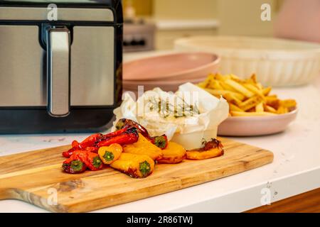 Roasted peppers, baked camembert, and potato chips all cooked in an air fryer, in a domestic kitchen. UK Stock Photo