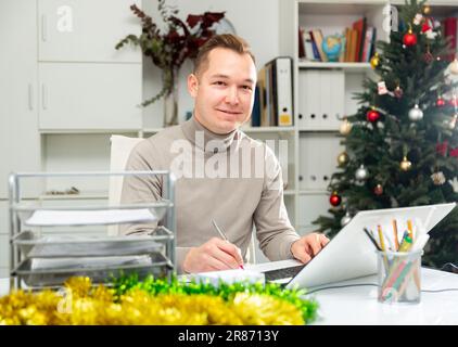 Cheerful man bookkeeper doing paperwork in Christmas decorated office Stock Photo