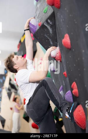Teenage boy climbs steep artificial wall in sports complex and trains endurance Stock Photo