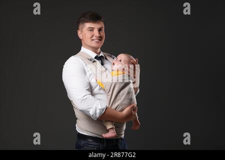 Father holding his child in baby carrier on black background Stock Photo