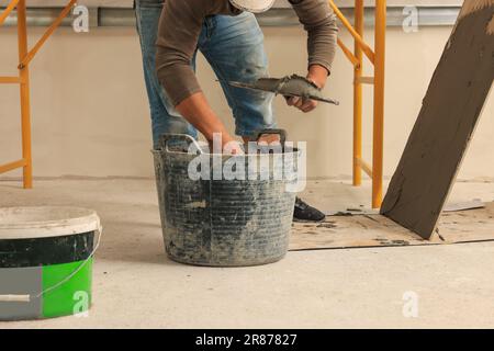 Worker applying adhesive mix on spatula near tile indoors, closeup Stock Photo