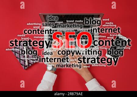 Search engine optimization (SEO). Cloud of words above copywriter with laptop against red background, top view Stock Photo