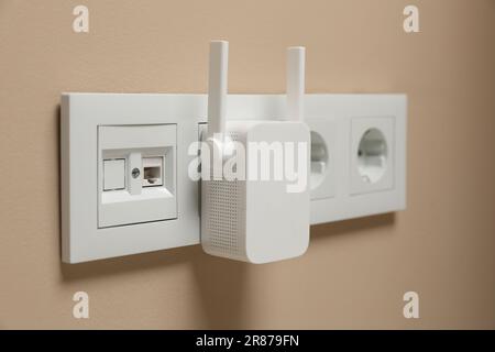 Wireless Wi-Fi repeater in power socket on beige wall Stock Photo