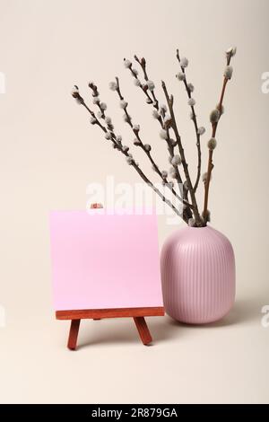 Vase with beautiful blooming willow branches and blank card on stand against beige background. Space for text Stock Photo