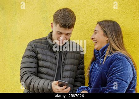 Latina girl laughing next to a caucasian boy on a yellow background. Stock Photo