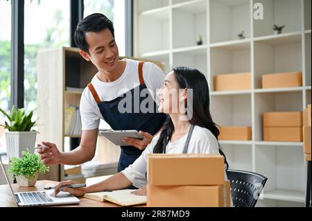 A lovely young Asian couple is discussing plans, checking online orders on the website, ordering products from their supplier through email, and worki Stock Photo