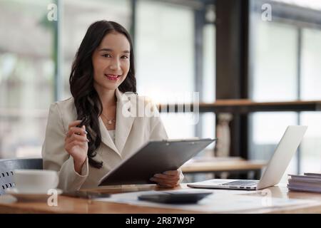 Financier a asian woman works, uses a laptop, makes a report to a finance company. Accounting and financial concept Stock Photo