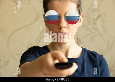 The flag of Russia on the glasses of the girl and in the hands of the remote control from the TV, Russia and propaganda from the TV, lies and deceptio Stock Photo