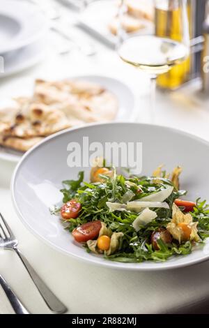 Rocket salad with parmesan, physalis and cherry tomatoes next to flat bread. Stock Photo