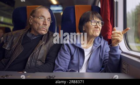 Elderly couple is riding in a train carriage and looking out the window and talking with each other Stock Photo