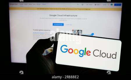 Person holding cellphone with logo of computing services Google Cloud Platform (GCP) on screen in front of webpage. Focus on phone display. Stock Photo