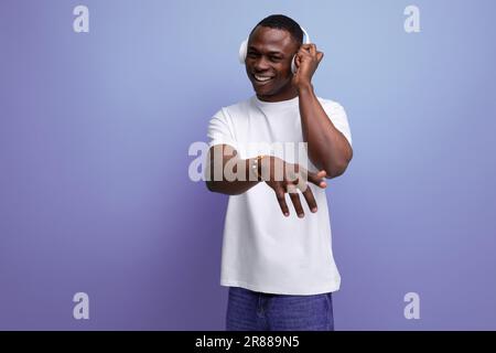 energetic joyful dark-skinned young american guy in a white t-shirt listens to a podcast in headphones Stock Photo